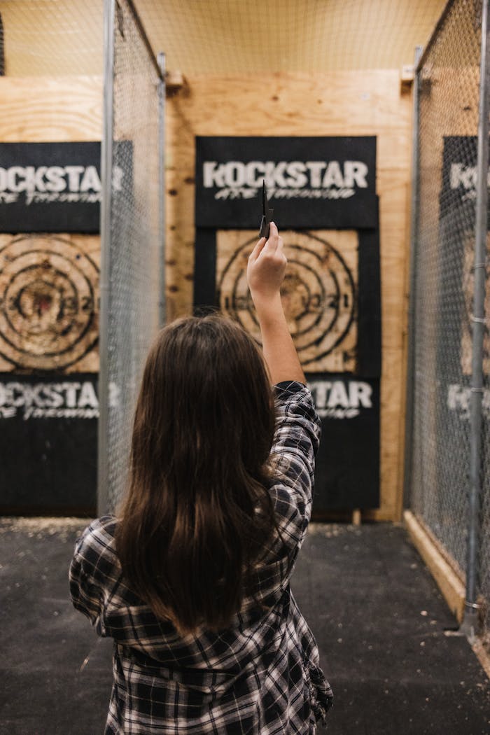 Crafting Captivating Headlines: Your awesome post title goes here Young woman throws an axe at a target in an indoor range, showcasing skill and focus.